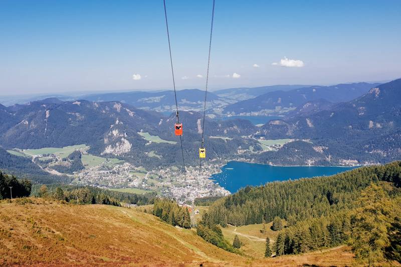 Cable cars travelling up and down Zwölferhorn mountain, with views of St. Gilgen below
